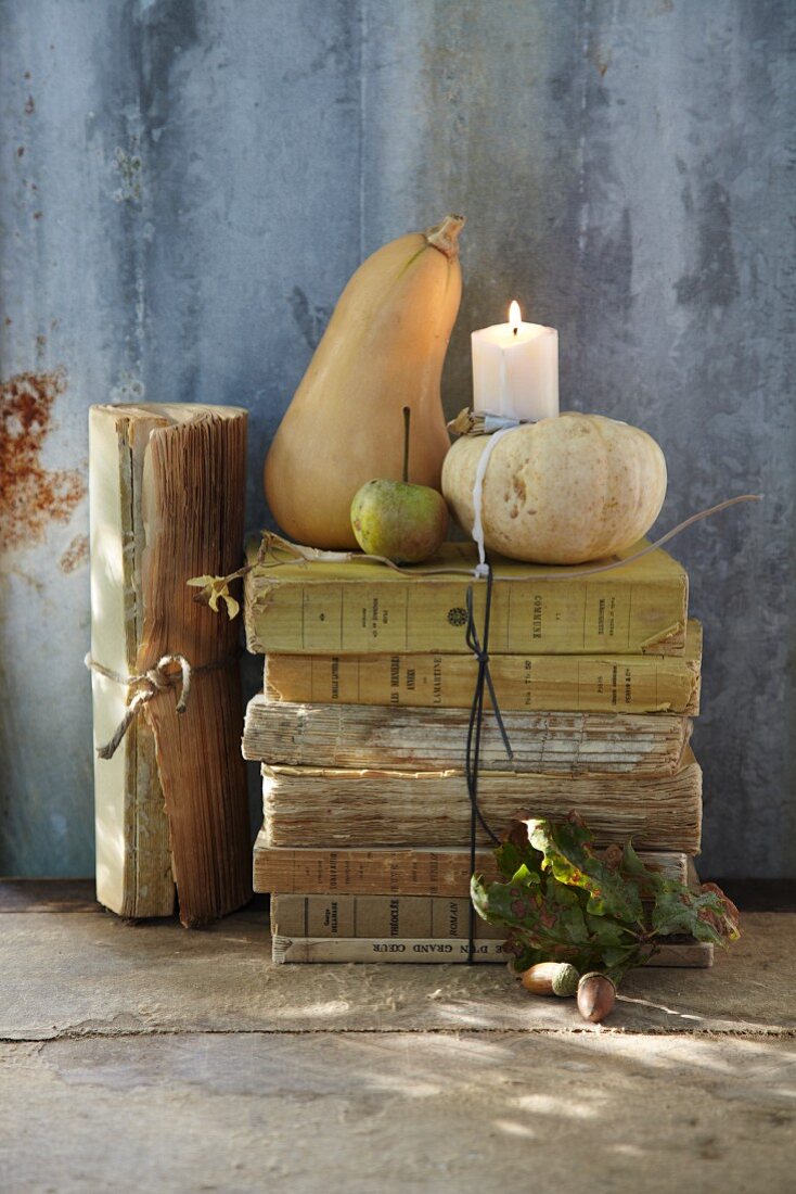 An autumnal arrangement of antique books, ornamental pumpkins and a candle