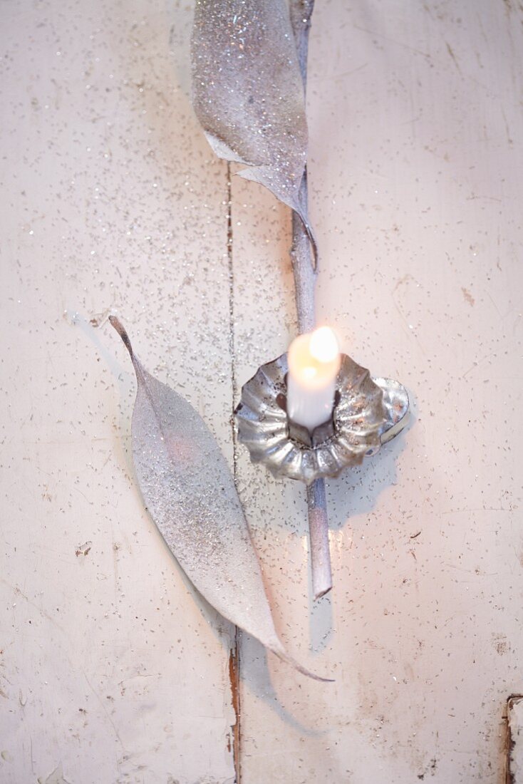 A Christmas tree candle, eucalyptus leaves and silver glitter as decorative material