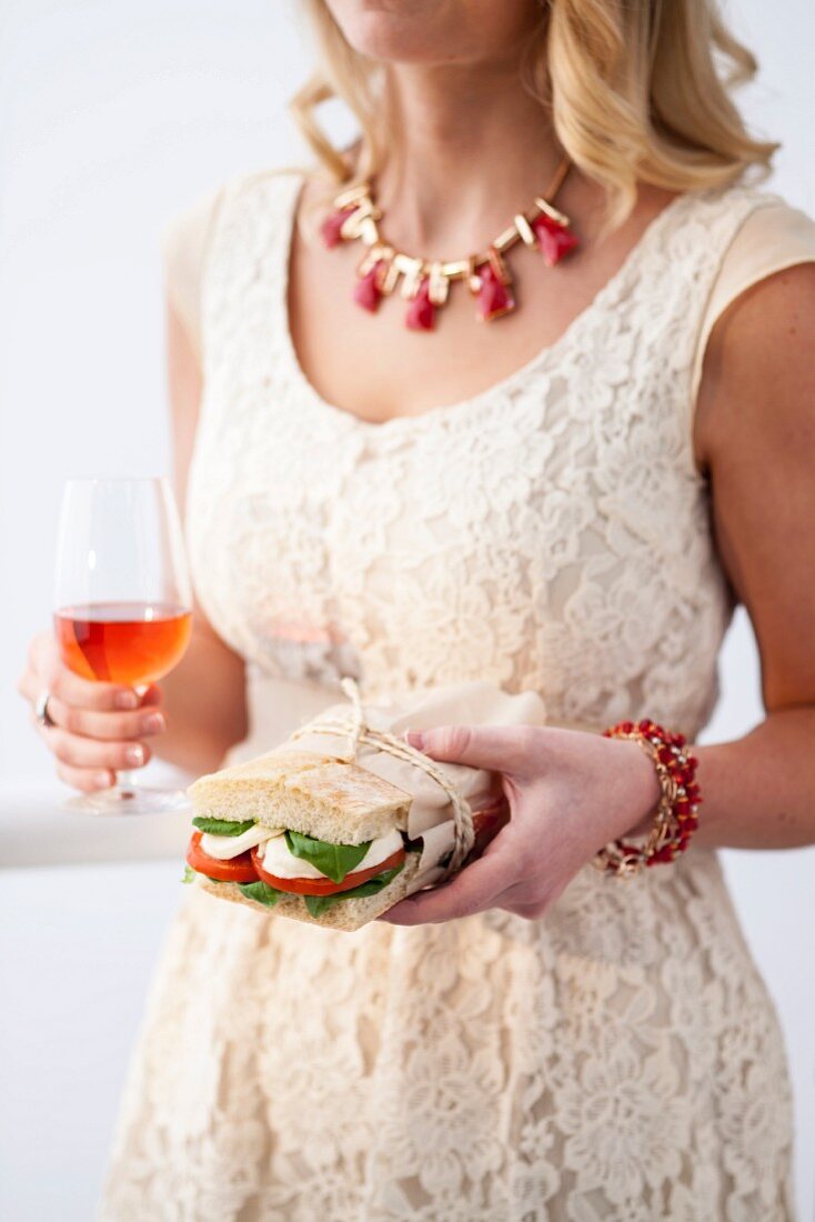 Junge Frau mit Tomaten-Mozzarella-Sandwich und Aperitif