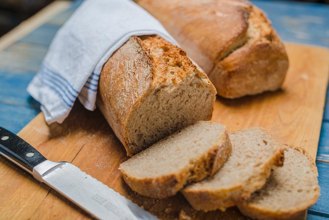 Sour dough bread on a chopping board with a knife (sliced)