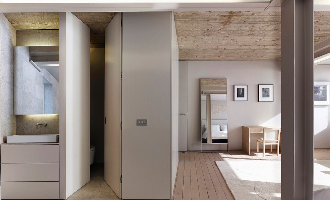 Washstand with drawers in base unit built into niche and separate toilet in spacious bedroom with exposed concrete ceiling and modern ambiance