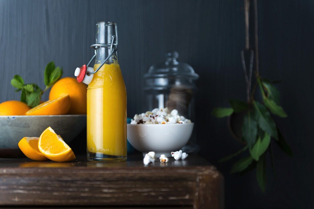 A bottle of orange juice, fresh oranges and popcorn