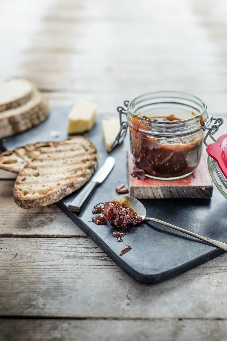 Tomato chutney in a jar and on a spoon, slices of bread and cheese