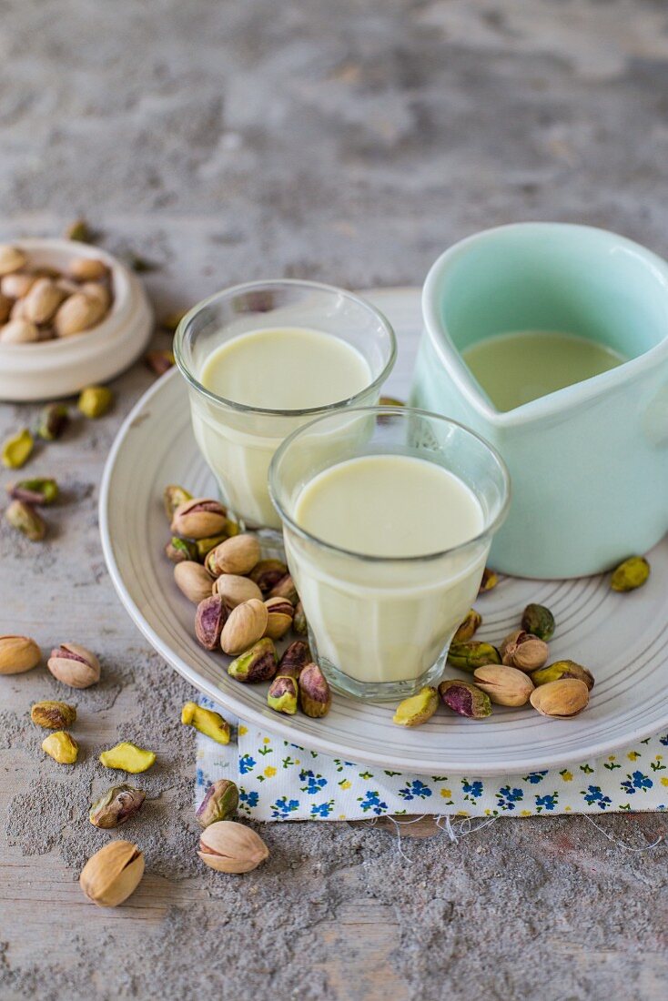 Pistachio milk in small glasses and a pastel blue jug with pistachios scattered around
