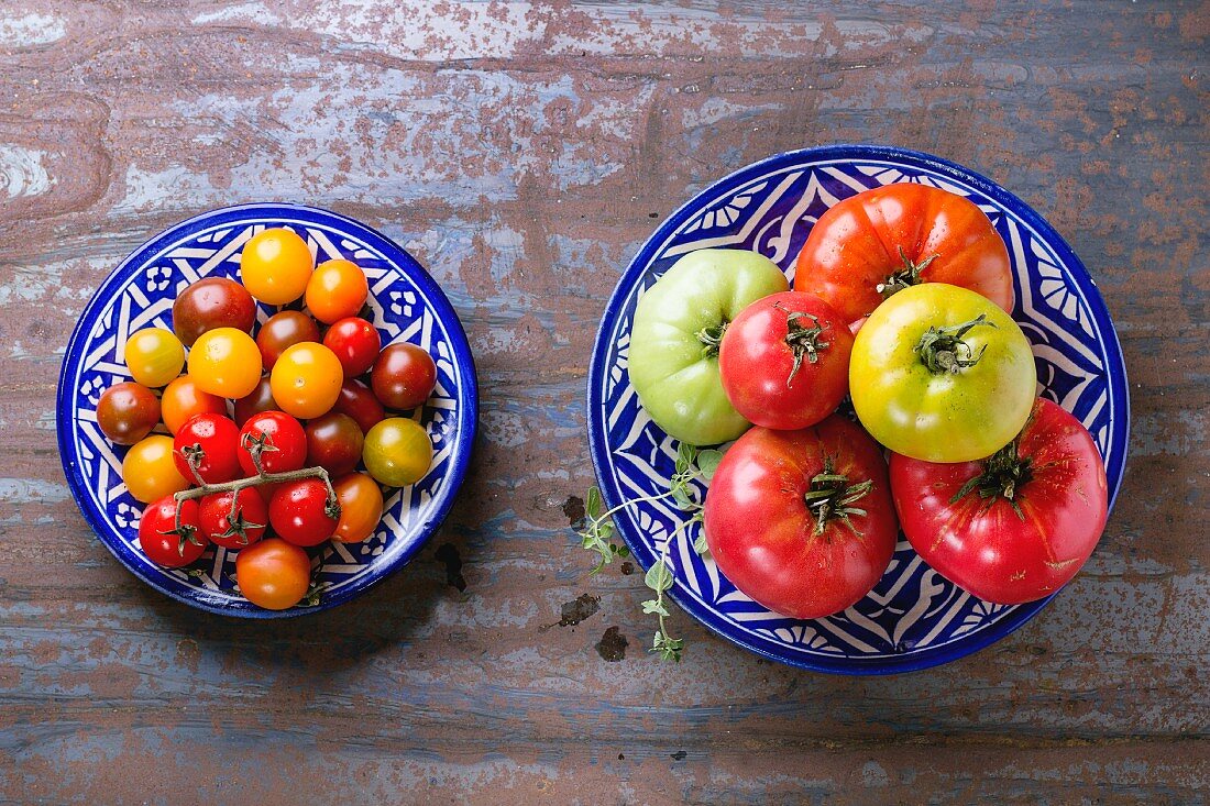 Zwei Teller mit verschiedenen Tomatensorten auf Metalluntergrund (Draufsicht)