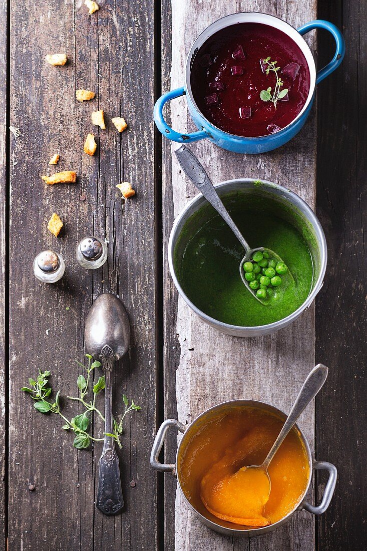 Three different types of cream soup (beetroot, pea and carrot) in old pots