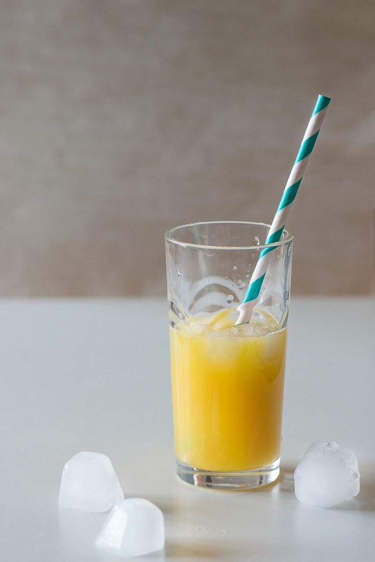 Glas Orangensaft mit Eiswürfeln und Retro-Strohhalm