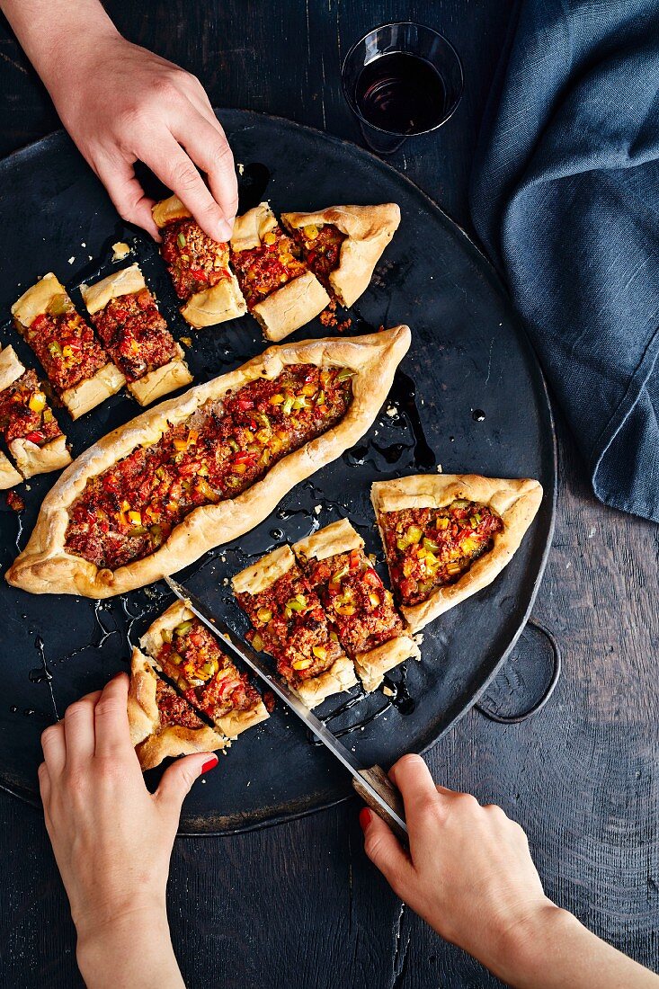 Hands taking Turkish pide with a minced meat and tomato filling