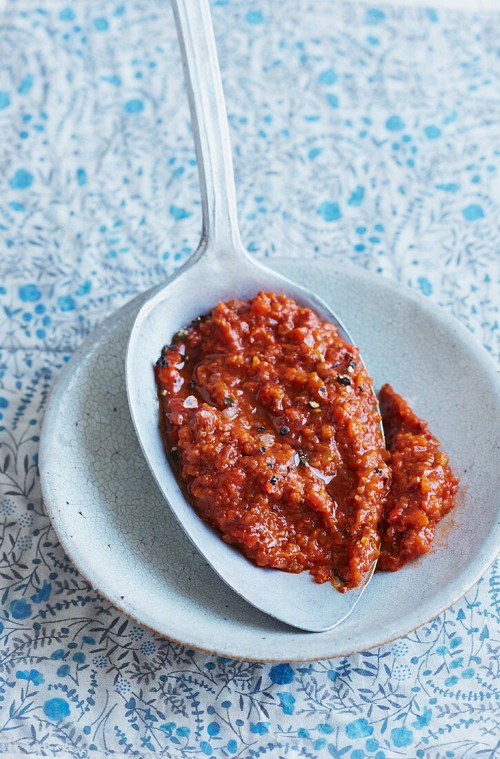 Pepper paste with unripe spelt grains and black olives on a spoon