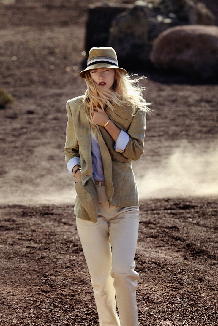 Blonde Frau mit Hut in sandfarbenem Sakko, blauer Bluse und beige Hose