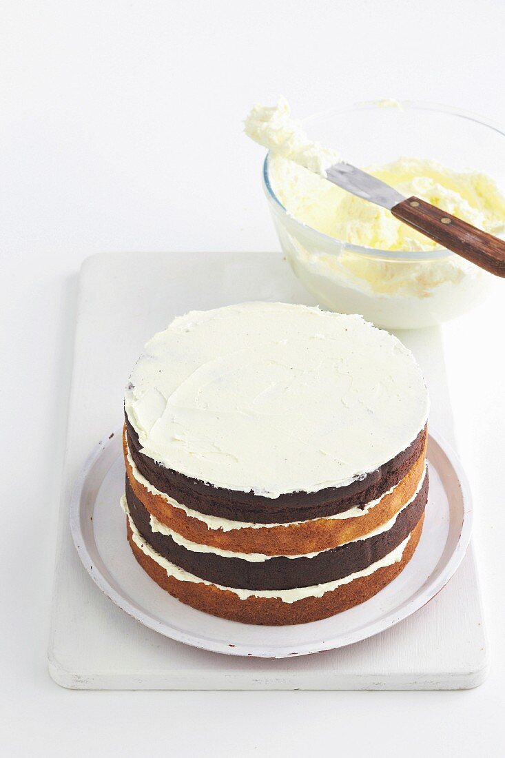 Eine Schwarz-weiss-Torte mit Buttercreme bestreichen