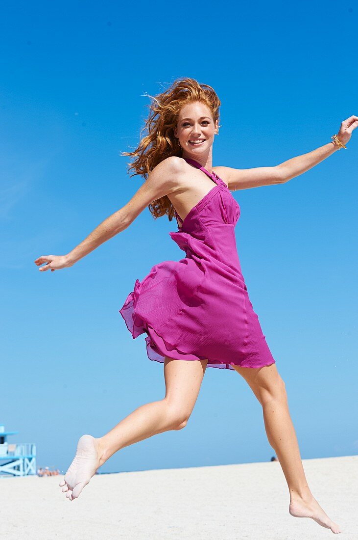 A happy young woman on a beach wearing a pink summer dress