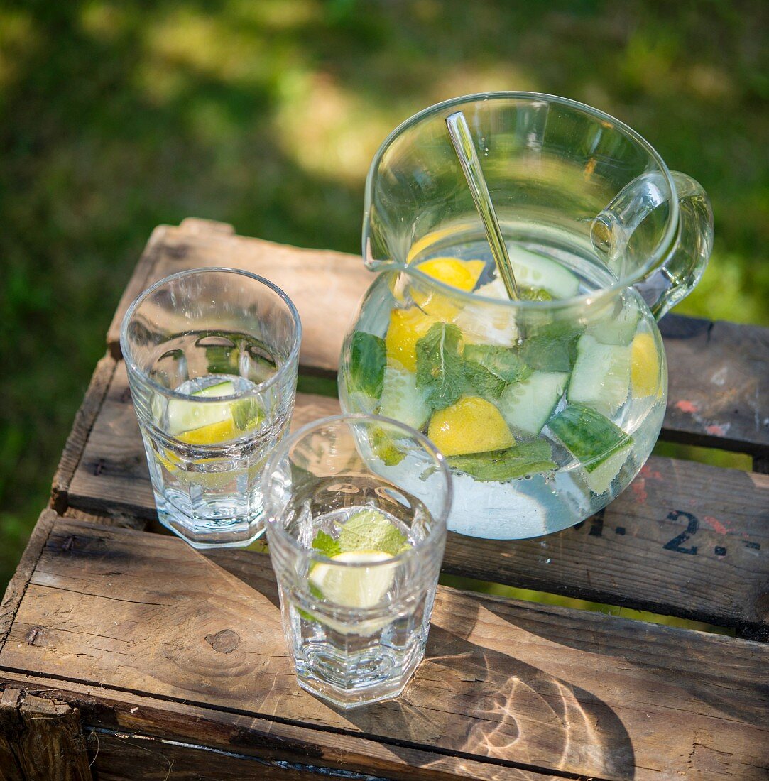 Lemon water with cucumber and mint on a wooden crate in the garden