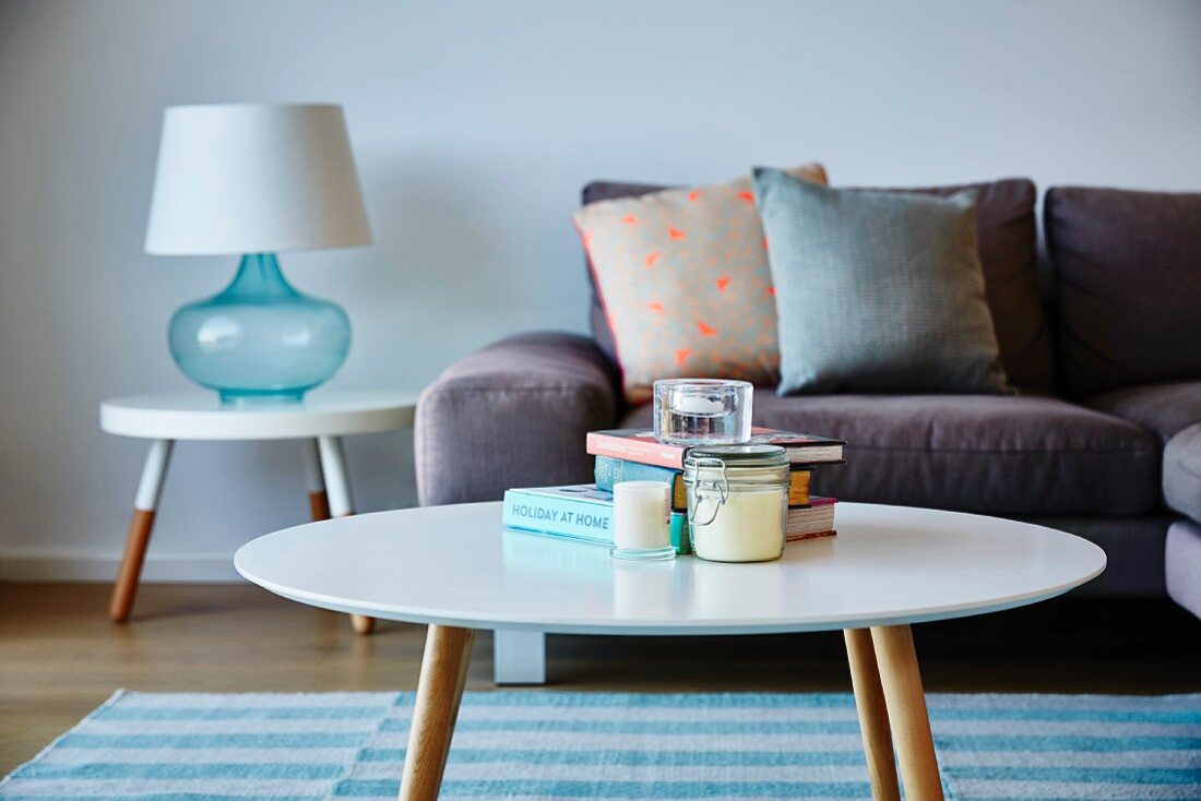 Round retro coffee table in front of sofa with scatter cushions and table lamp on side table