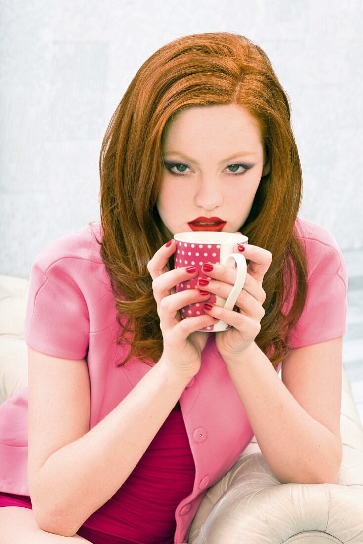 Rothaarige Frau in pinkfarbener Bekleidung mit Kaffeebecher