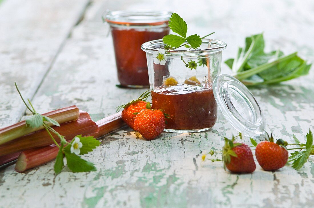 Erdbeer-Rhabarber-Marmelade in Gläsern, frische Erdbeeren, Rhabarber und Erdbeerblüten auf Holztisch