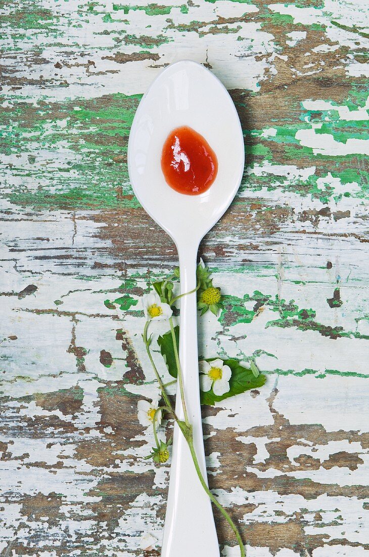 Strawberry jam on a spoon and strawberry flowers on a wooden table