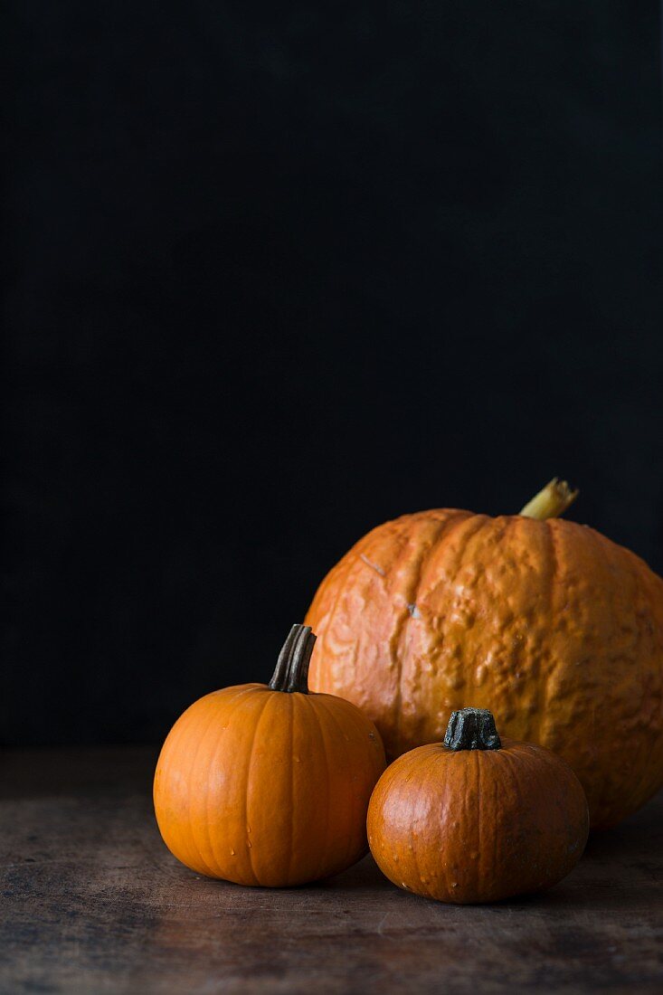Three pumpkins of various sizes against a dark background