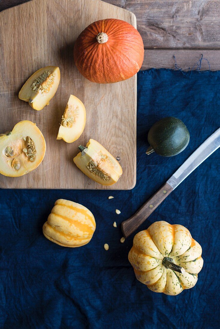 Various pumpkins, partially sliced, on a chopping board and a blue cloth