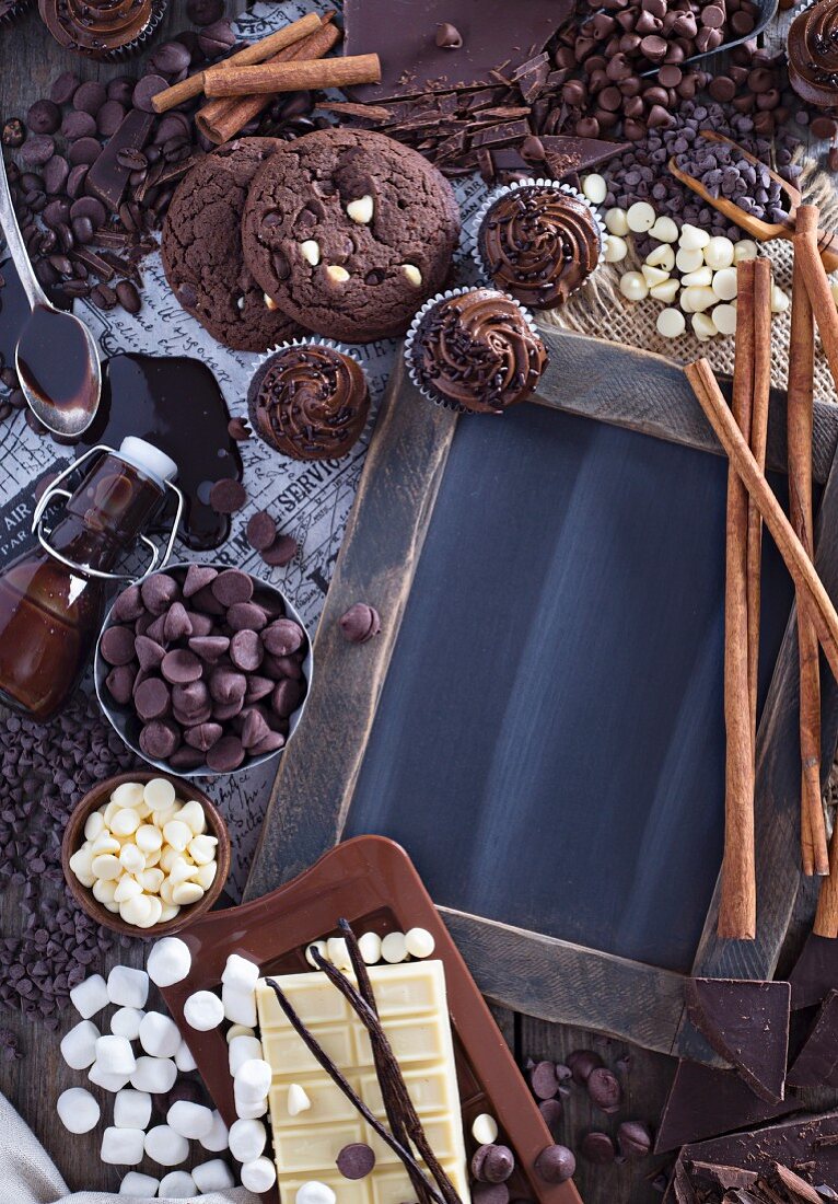 Schokoladenstilleben mit Cookies, Cupcakes, Chocolatechips, Sirup, Marshmallows und Zimtstangen