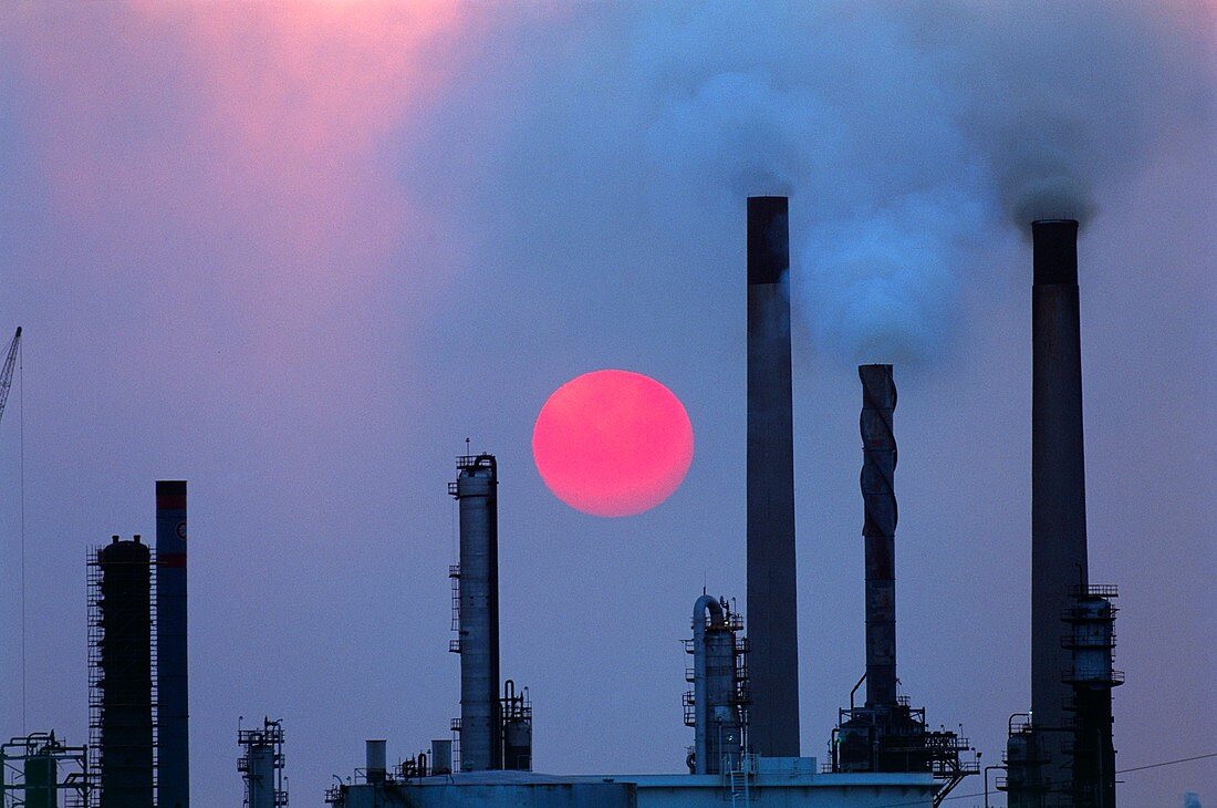 Smoking chimneys of an oil refinery at sunset