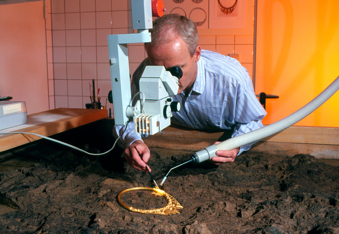 Archaeologist cleaning a golden Celtic necklace