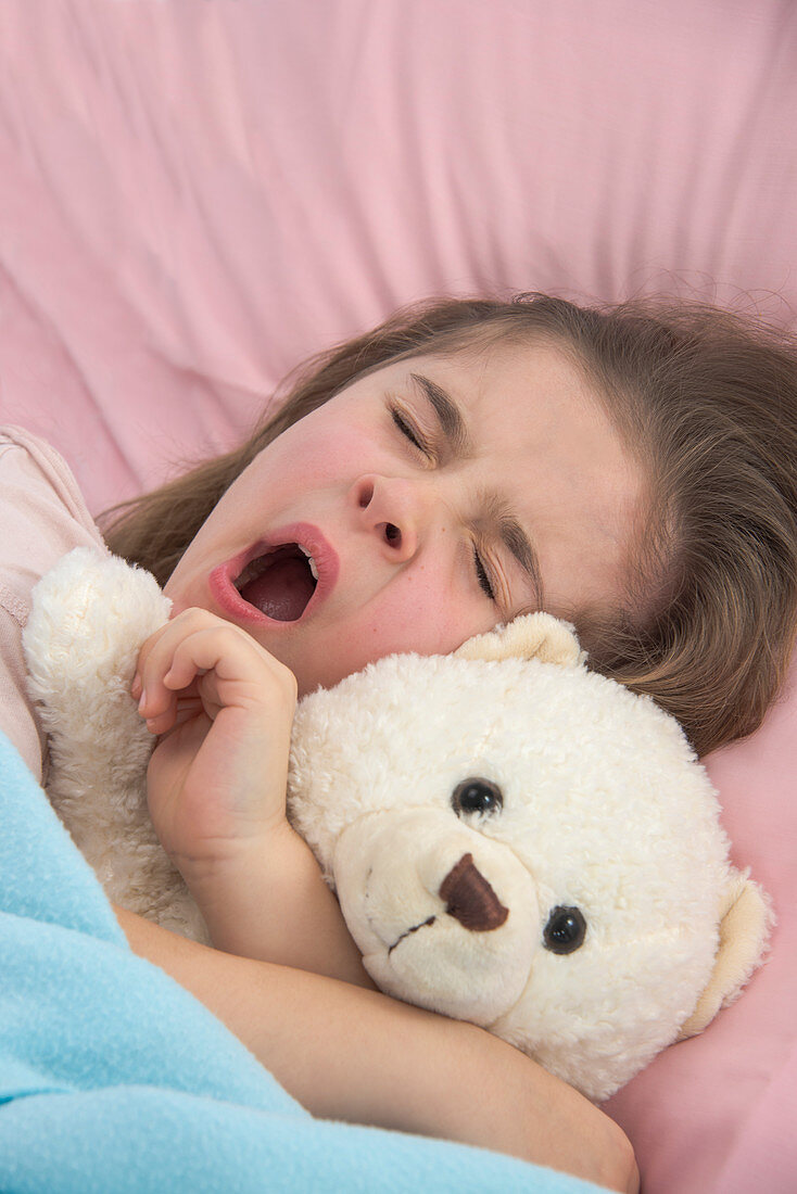 Girl yawning in bed holding teddy bear