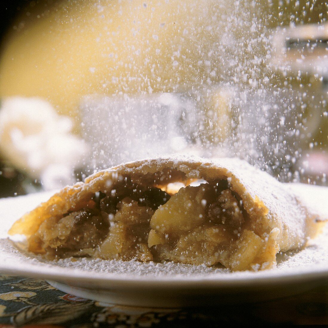 A piece of apple strudel being sprinkled with icing sugar