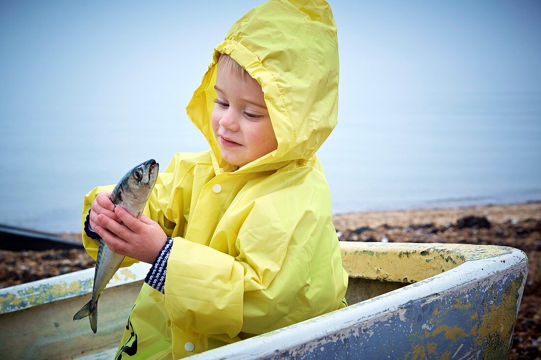 Boy wearing raincoat holding a mackerel