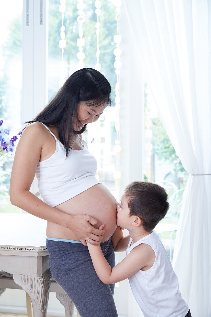 Pregnant woman with son kissing her tummy