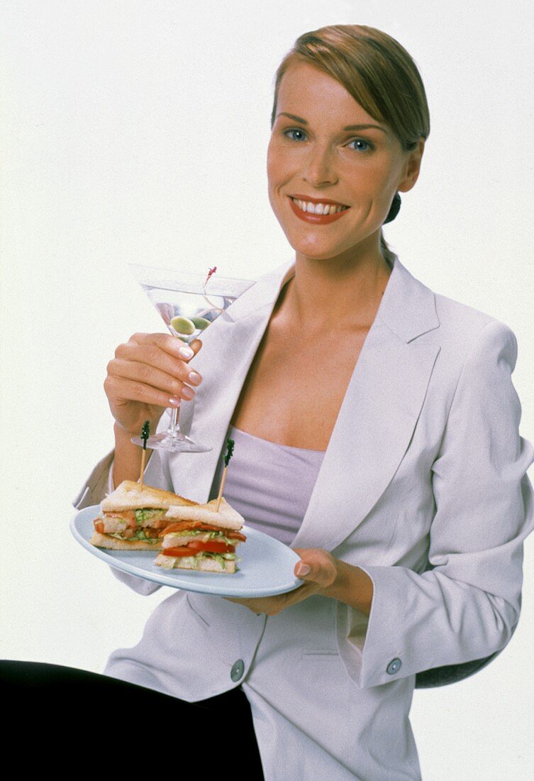 Junge Frau im weißem Blazer hält Martiniglas & Sandwiches