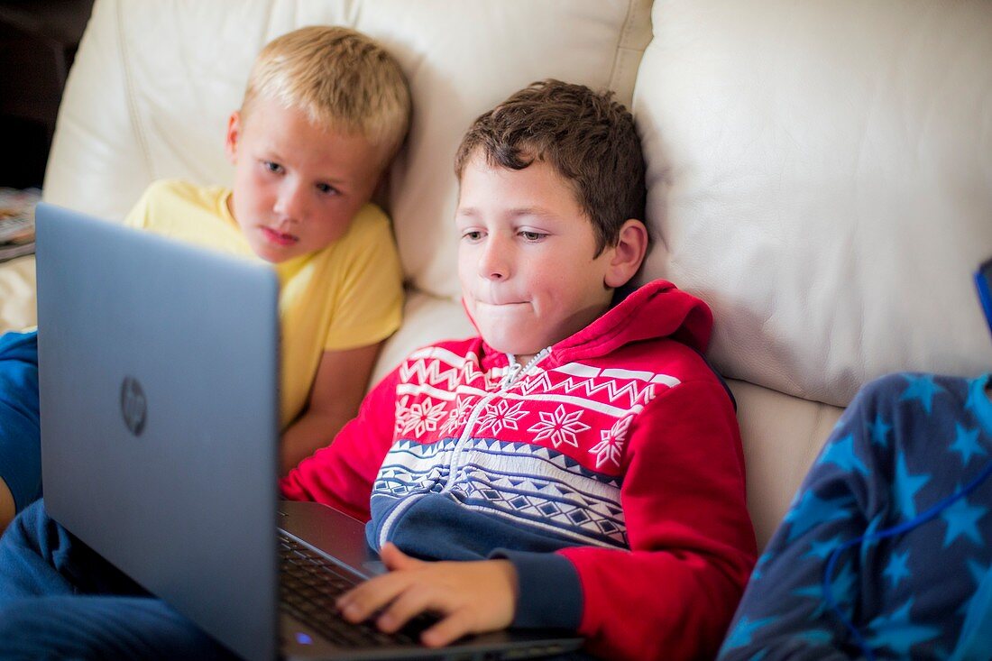Two boys using a laptop sitting on sofa
