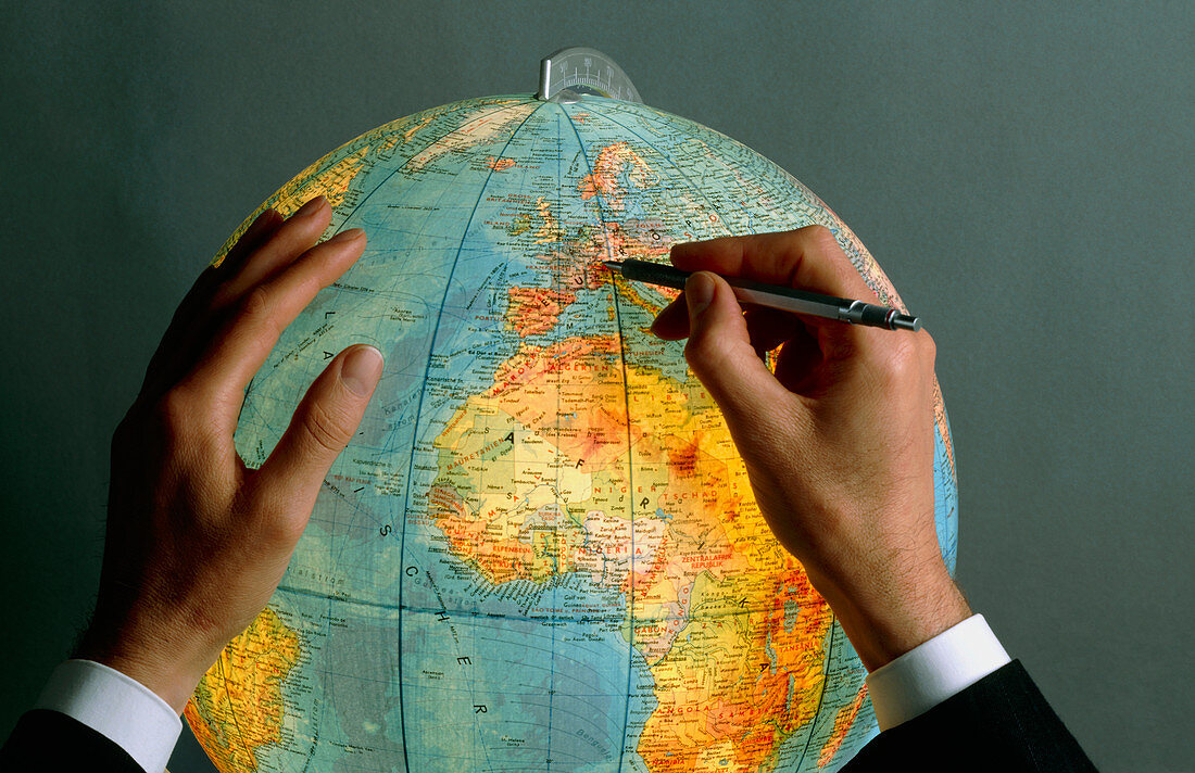 Man pointing to a position on a globe with a pen