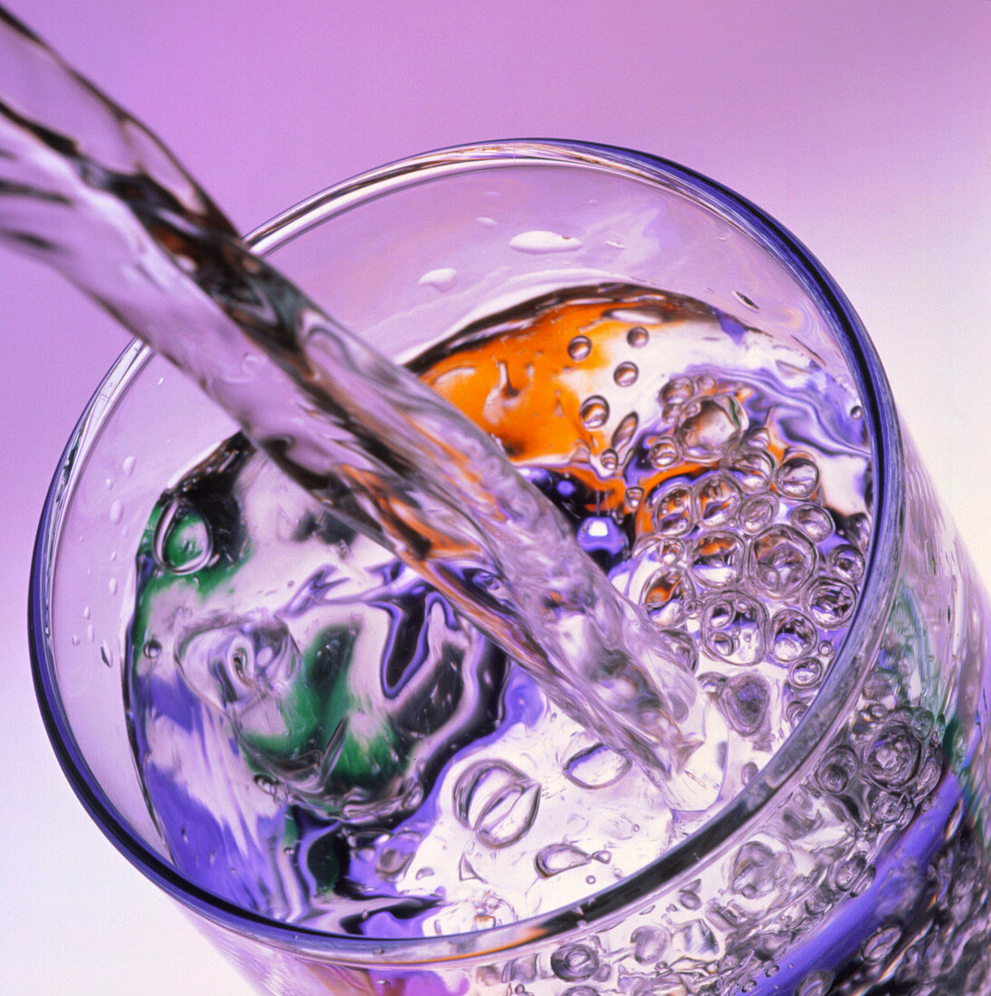 Water streaming into glass,mauve background
