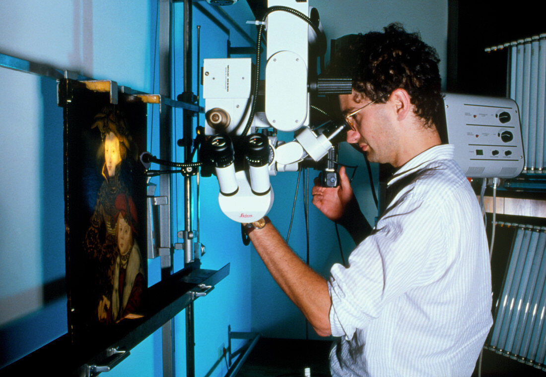 Technician examines forged painting by microscope