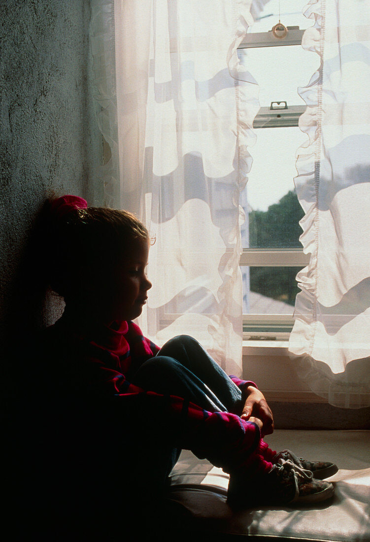 Lonely young girl sitting by a window