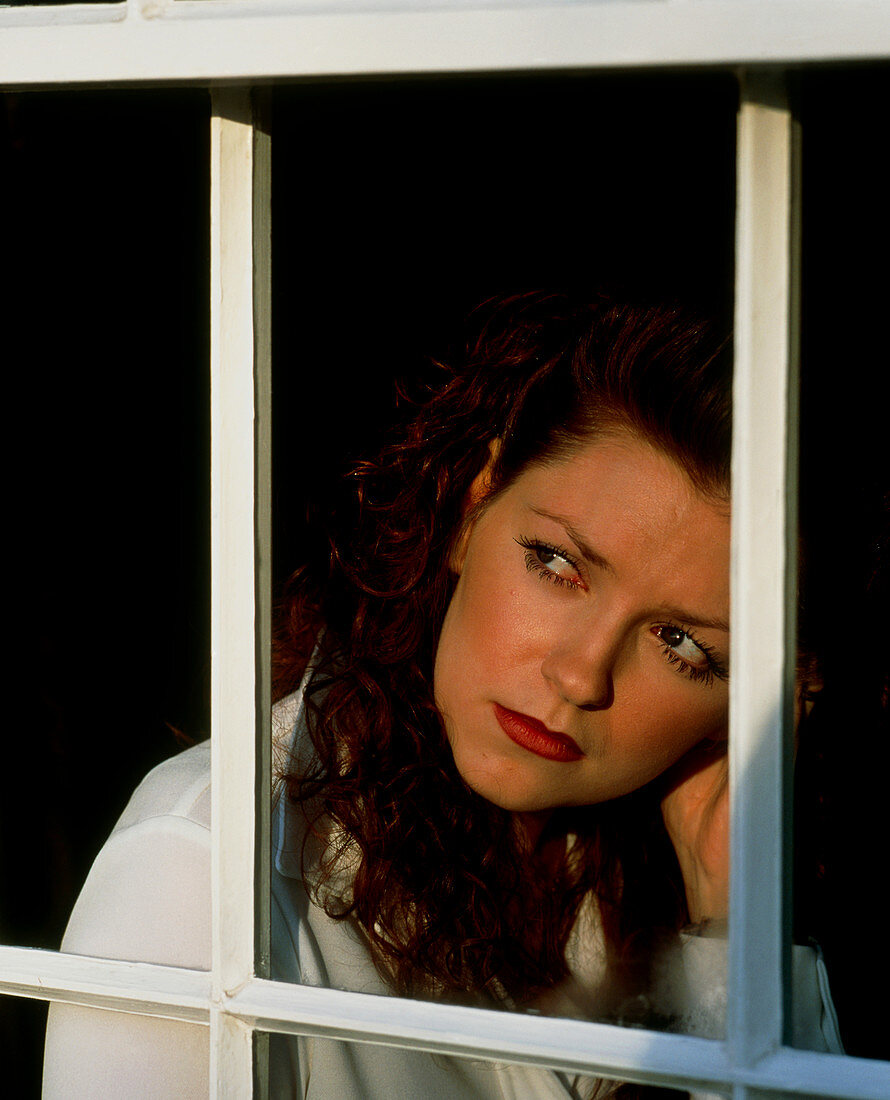 A depressed young woman stares out of a window