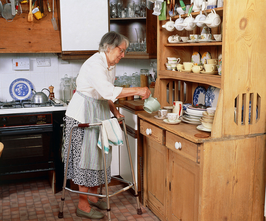 Elderly woman with zimmer frame makes cup of tea