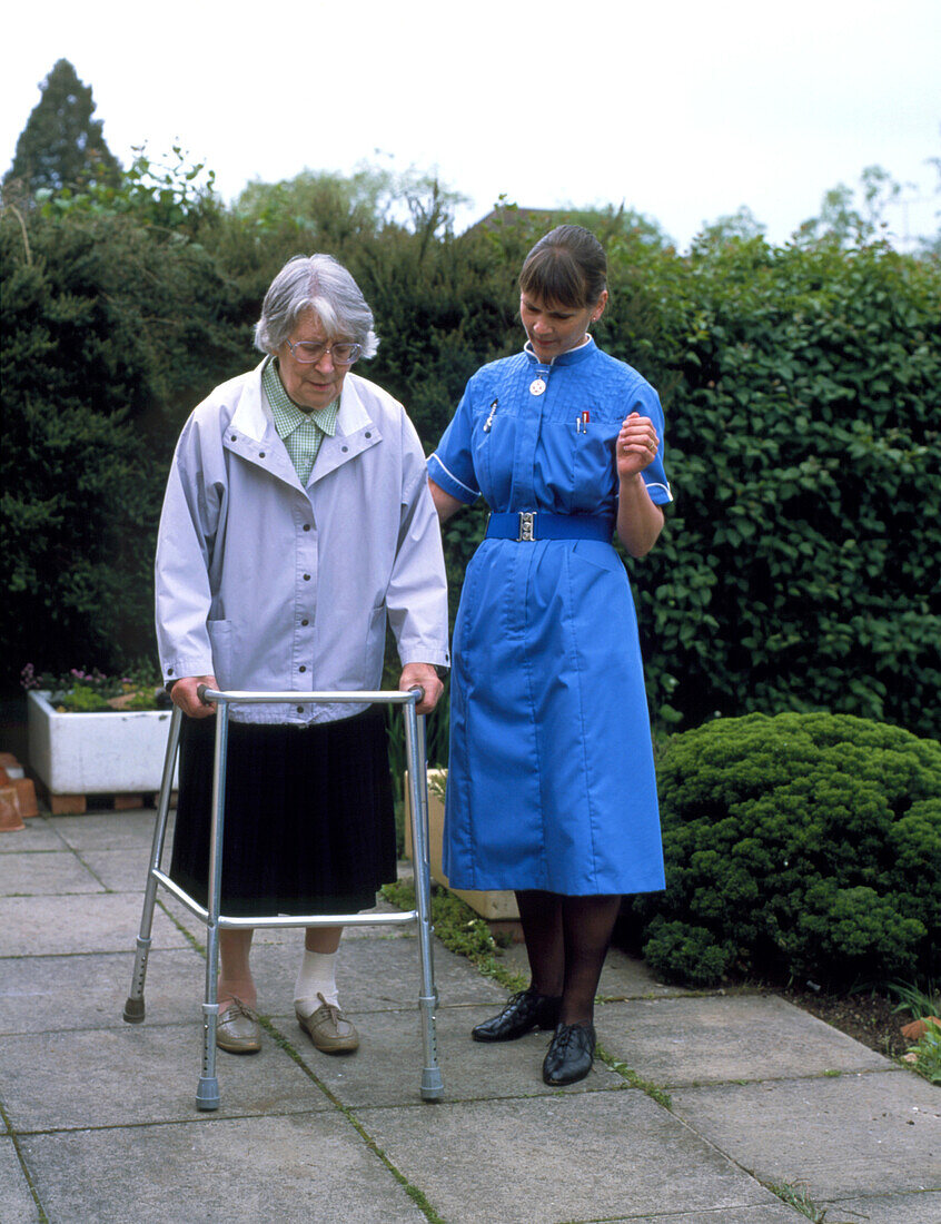 District nurse helps old woman use walking frame