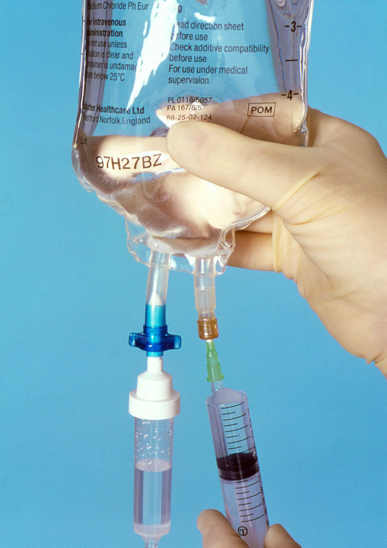 Gloved hands injecting a drug into an IV drip bag