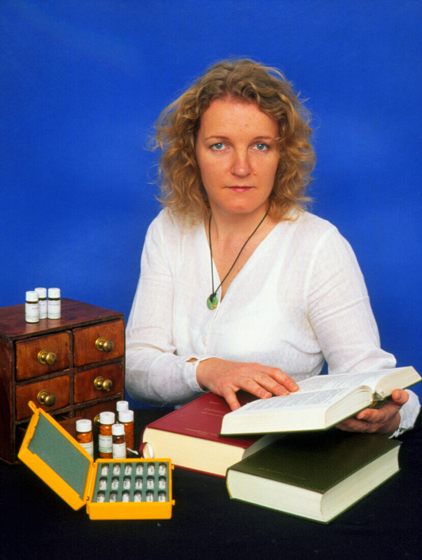 Homeopath with book beside selection of medication