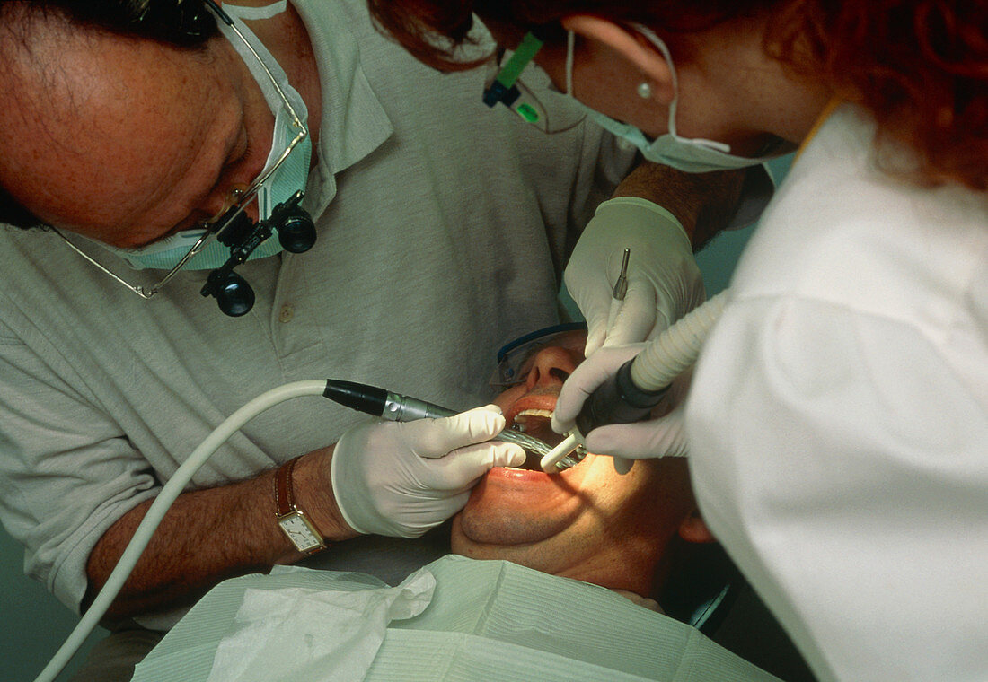 Dentist and assistant drilling a man's teeth