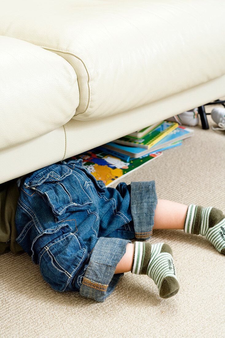Toddler crawling beneath a sofa