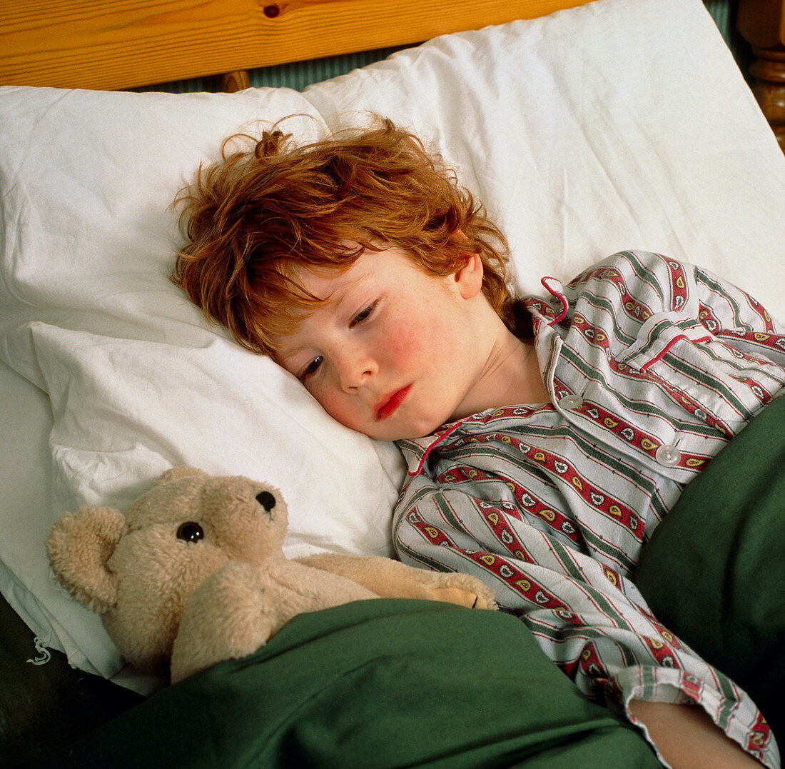 Feverish child in bed with teddy bear