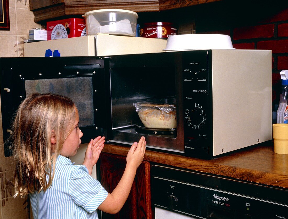 Child danger: young girl takes food from microwave