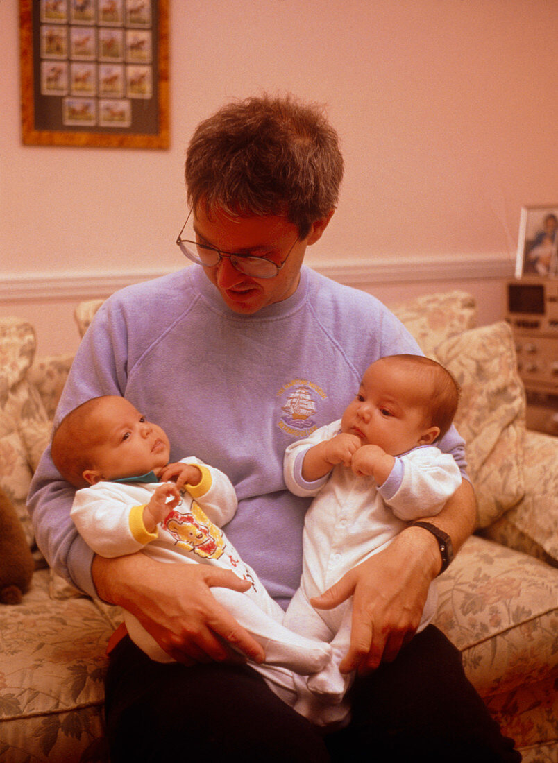 Infant identical twins being held by their father