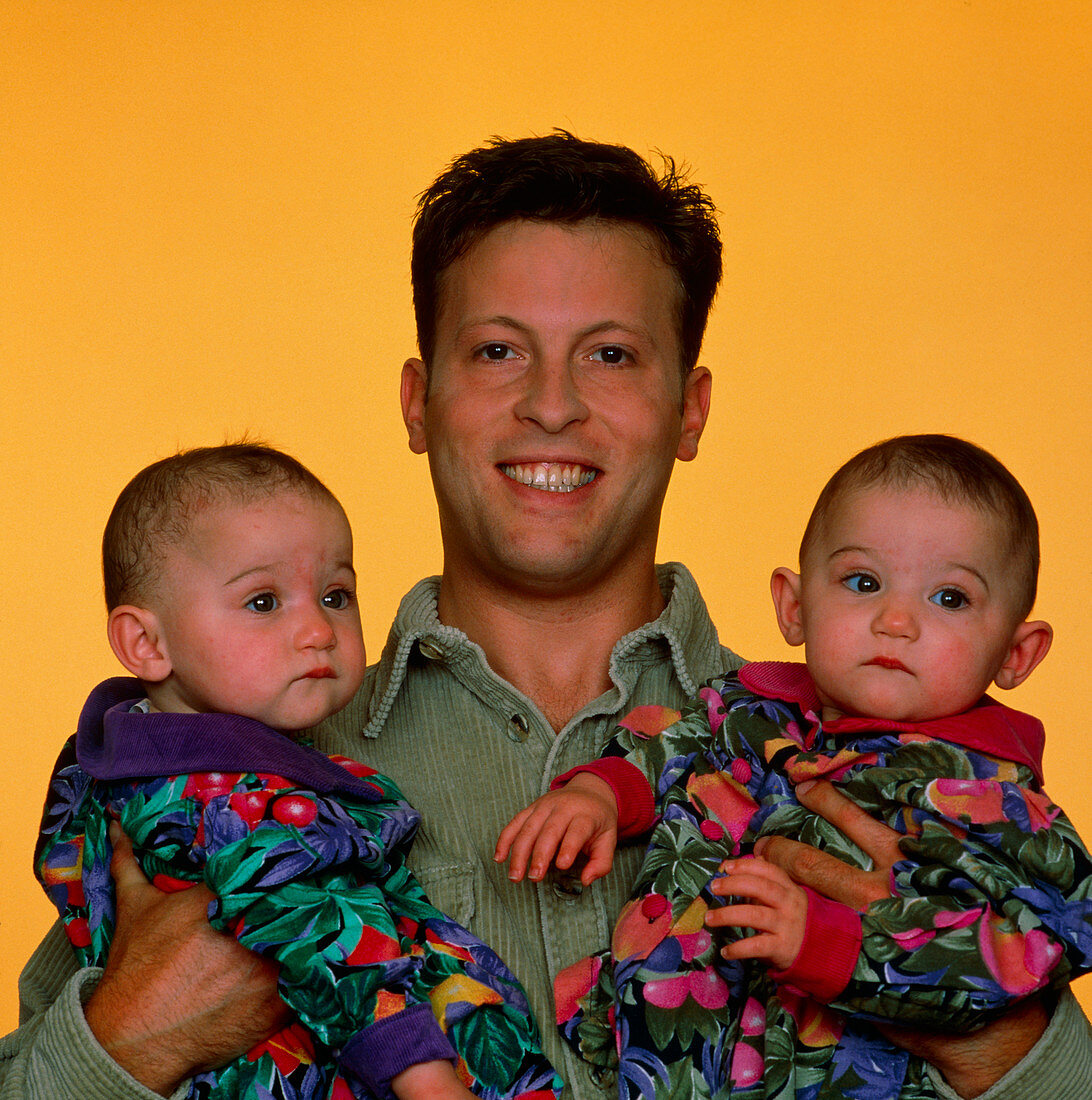 Infant identical twins being held by proud father