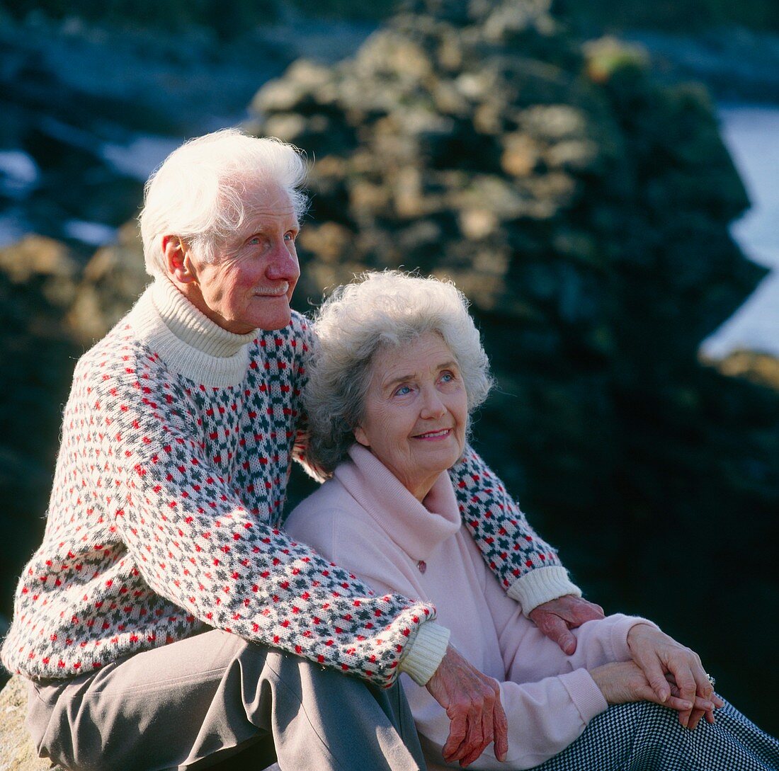 Elderly couple sit together at a rocky coast