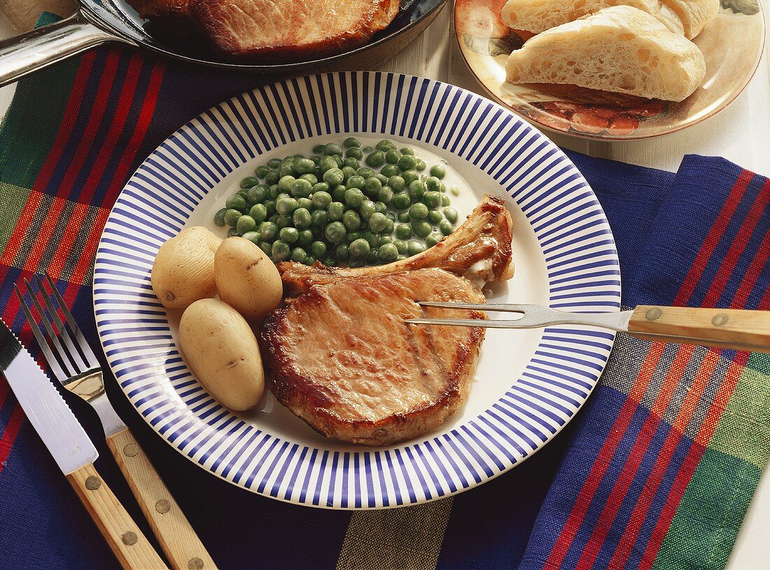 Schweinekotelett mit Sahneerbsen & Pellkartoffeln auf Teller