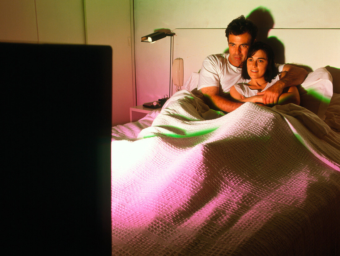 Man and woman watch television in bed